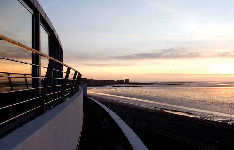 Sunset view of the Midland Hotel, its iconic Art Deco silhouette reflected in the waters of Morecambe Bay, creating a dramatic seaside scene.